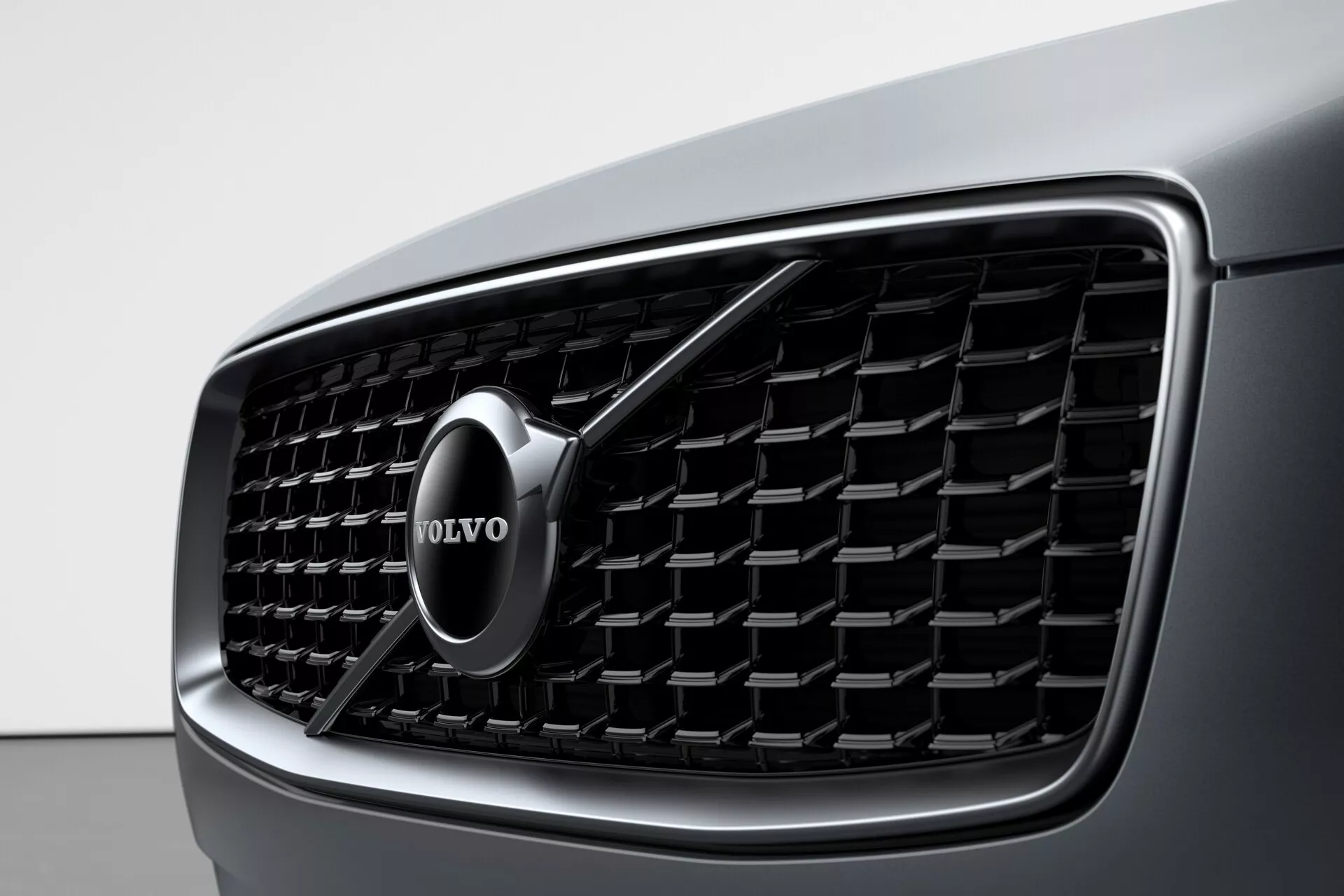 Detailní pohled na přední masku vozu Volvo XC90 2015 (2. generace) s důrazem na podrobný design a výrazný znak značky Volvo. Maska má vertikální lamely a chromový okraj, což zdůrazňuje luxus a moderní estetiku.