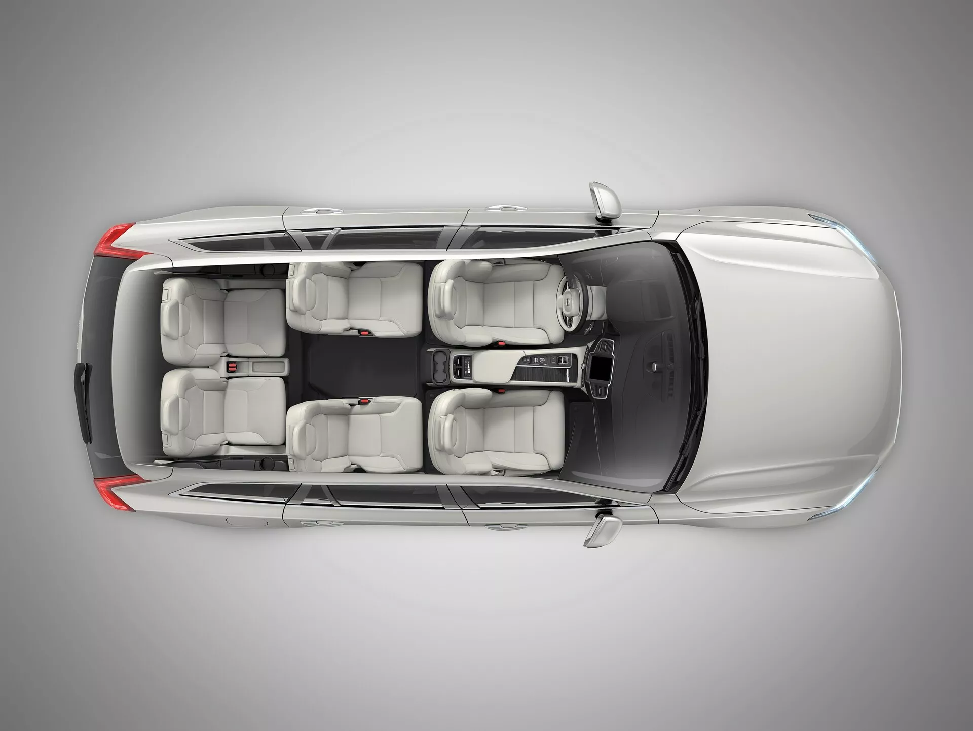 Pohled shora na Volvo XC90 2015 (2. generace) ukazující jeho stříbrně metalickou šedou exteriér, čtyřdveřový karoserii SUV, okna s tónovanou UV ochranou, interiér sedmimístný se světle šedými sedadly a kola z lehkých slitin. Obrázek zdůrazňuje funkce jako ADAS, bezpečnost vozidla, informační systém, vícezónovou klimatizaci, bezklíčový vstup a parkovací asistenční systémy, s ateliérovým osvětlením zajišťujícím jasné zaměření na detaily designu.