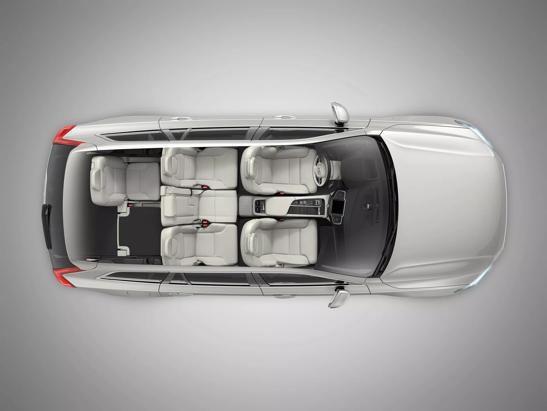 Letecký pohled shora na dobře udržovaný stříbrný sedan Volvo XC90 druhé generace z roku 2015. Obrázek zachycuje celou délku a šířku vozu, ukazuje celou střechu, karoserii a okolí. Všechna okna a dveře jsou zavřeny, kliky dveří hladce zapadají do designu, zpětná zrcátka jsou zasunuta. Střecha nemá střešní okno a lak je rovnoměrně lesklý. Interiér je viditelný skrze průhlednou střechu, zdůrazňuje béžové nebo světle šedé čalounění, dvě řady sedadel s opěrkami hlavy a standardní pneumatiky. Tvar krytů koncových a předních světel je viditelný, ale nedetailní.