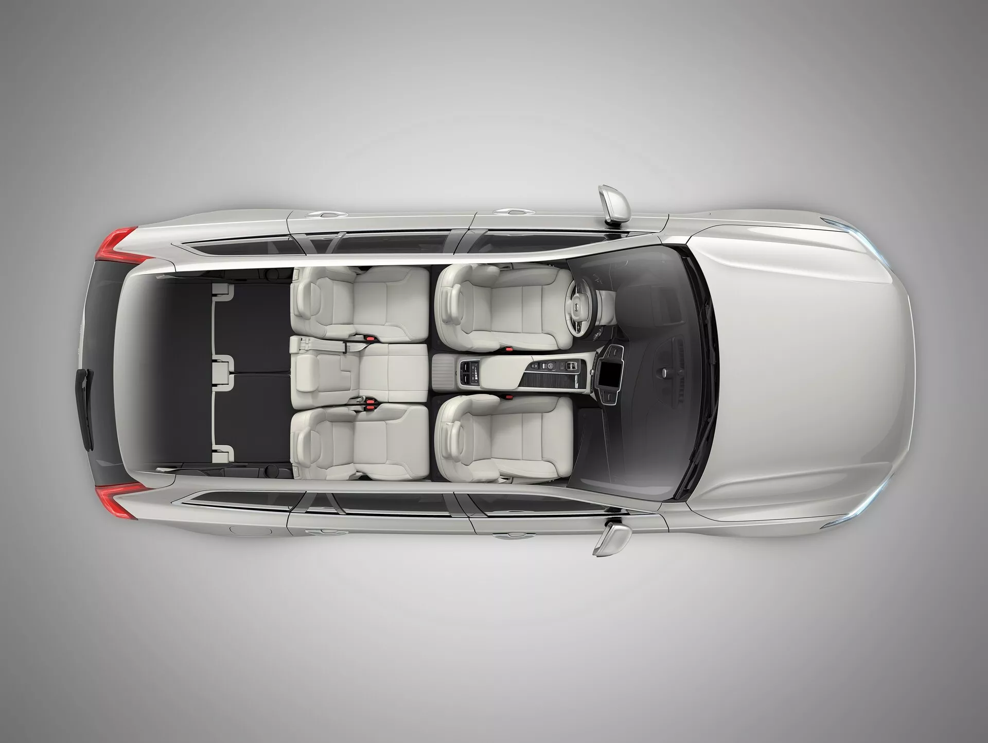 Pohled shora na kovový Volvo XC90 2015 ukazující kontrastní černou střechu, aerodynamický design, střešní okno, dvě řady sedadel s pokročilými nastavitelnými předními sedadly, centrální ovládací konzoli a tónovaná okna, uprostřed profesionálního studia.
