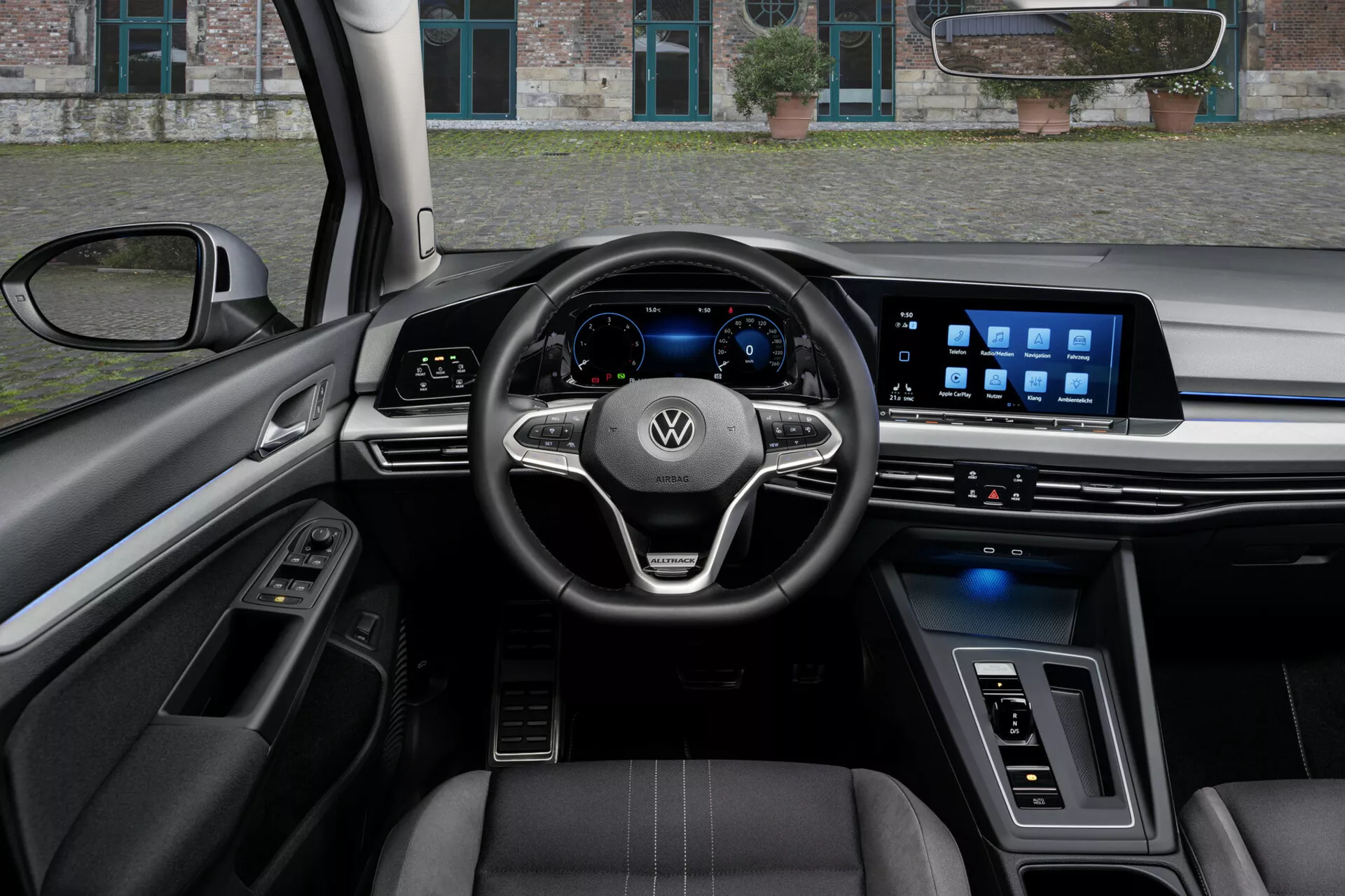 Interiér VW Golf Alltrack 2017 z pohledu řidiče, zobrazuje volant se třemi rameny s ovládacími prvky a logem Volkswagen, digitální přístrojový panel a široký dotykový infotainment systém na palubní desce, zvýrazněný pokročilými technologickými funkcemi, sedadla potažená kůží s kontrastním prošíváním a kombinací luxusních materiálů a ambientního osvětlení.