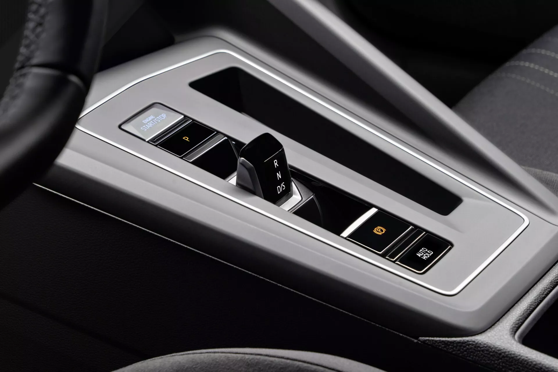 Detailní pohled na středovou konzolu VW Golf Alltrack 2017, zdůrazňující automatickou převodovku se zařazovací pákou v lesklém kovovém rámečku s elektronickým displejem, obklopenou černou kůží nebo syntetickou kůží, s indikátory zařazených rychlostí, sportovním režimem a pokročilými tlačítky pro asistenci řidiče.