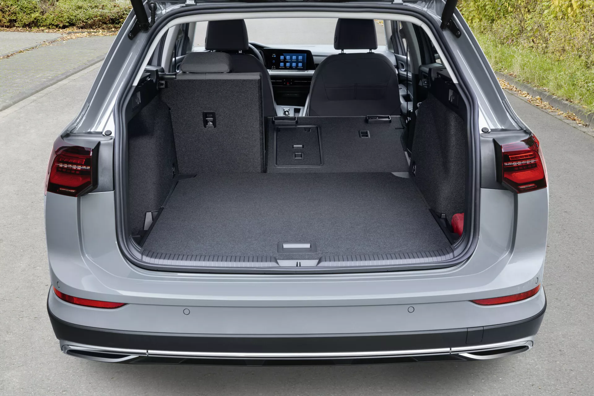Pohled shora na zadní nákladový prostor VW Golf Alltrack z roku 2017 s otevřeným poklopem, zobrazující plochou nákladní plochu se sklopenými zadními sedadly, LED zadní světla, parkovací senzory na zadním nárazníku a náznaky moderní technologie infotainmentu skrze zadní část.