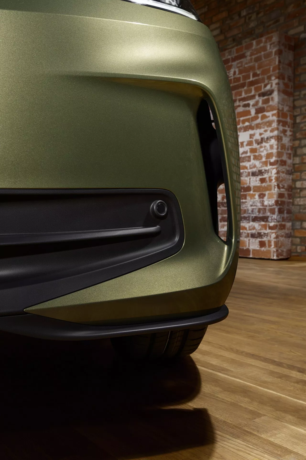 Detailní pohled na facelift VW ID.3 první generace r.v. 2023 s matně olivově zeleným povrchem, zaměřený na aerodynamický přední nárazník a ventilační otvor, integrovaný parkovací senzor, v expozici showroomu zdůrazňující jeho výkon a pokročilé designové prvky.