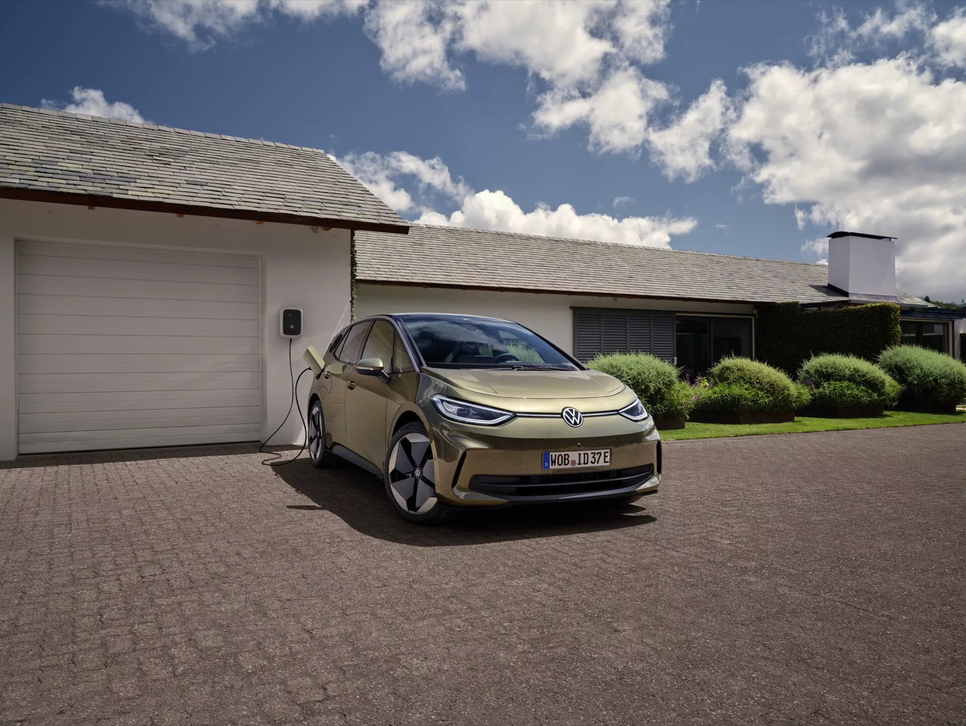 VW ID.3 1. generace facelift, elektrické vozidlo (EV) nabíjené před obytnou garáží, prezentující moderní design se štíhlými liniemi, charakteristickými LED světlomety, aerodynamickými prvky a možností domácího nabíjení, umístěné v předměstském prostředí.