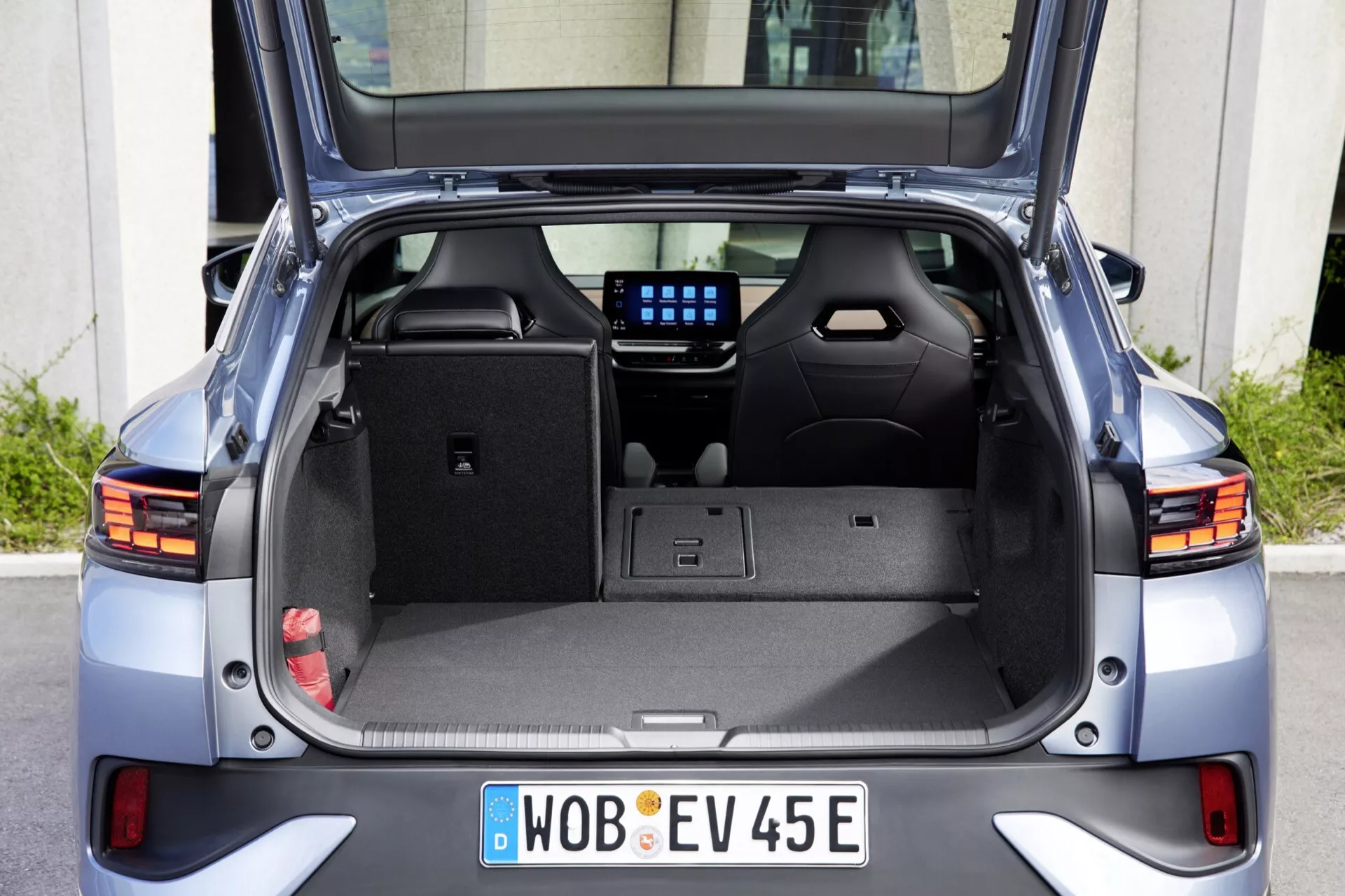 Pohled zezadu na Volkswagen ID.5 2022 (1. generace) zobrazující otevřený kufr, který jasně ilustruje interiér nákladu, zadní kabinu, zadní světla, zadní nárazník a stěrač zadního okna. Fotografie zdůrazňuje prázdný prostor kufru s háčky, přihrádkami, 12V zásuvkou a digitálním displejem mezi zadními sedadly, který nabízí pohled na infotainment nebo klimatizační systém vozidla.