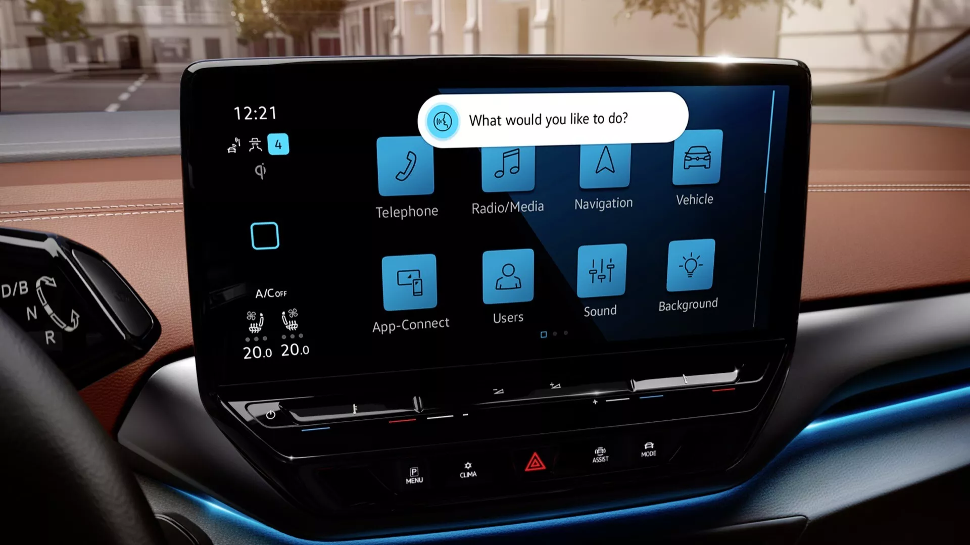 Tento obrázek ukazuje interiér modelu 2022 VW ID.5 (1. generace), konkrétně se zaměřuje na centrální dotykovou obrazovku infotainmentu. Záběr z pohledu sedícího na předním sedadle pasažéra nebo řidiče zdůrazňuje moderní displej s vysokým rozlišením. Obrazovka je v horizontální orientaci a obklopená minimálním množstvím fyzických tlačítek, přičemž obsahuje uživatelsky přívětivé rozhraní s velkými ikonami pro Telefon, Rádio/Media, Navigaci, Nastavení vozidla, App-Connect, Uživatelské profily, Nastavení zvuku a Nastavení pozadí. Obrazovka také zobrazuje duální automatickou klimatizaci nastavenou na 'lo' pro obě strany a čas ve 12:21. Pod obrazovkou jsou několik fyzických tlačítek pro rychlý přístup k základním funkcím. Rozmazaná horní část přístrojové desky a modré ambientní osvětlení v dolní části přístrojové desky zdůrazňují prémiový interiér. Rozmazané pozadí za čelním sklem naznačuje městské prostředí.