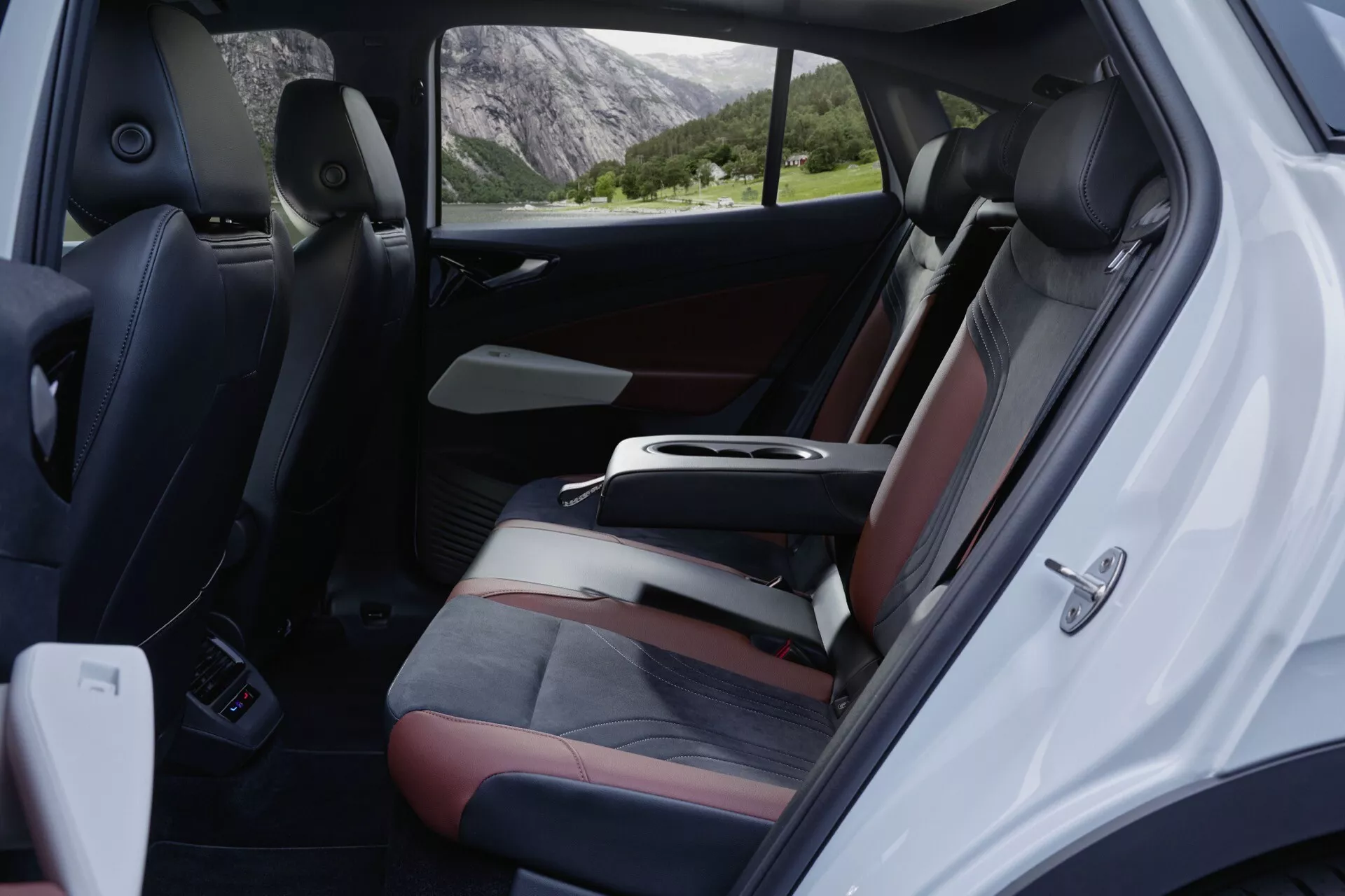 Pohled do interiéru vozu Volkswagen ID.5 z roku 2022 (první generace) zachycující zadní pasažérský prostor z pravého úhlu, s důrazem na prostorná dvoubarevná sedadla s tmavým a světlým čalouněním, dobře integrovanou středovou konzoli a otevřené pravé zadní pasažérské dveře zobrazující ovládací prvky elektrických oken, zamykání dveří, mřížky reproduktorů a kapsu na uložení. Viditelná je také upravená podlaha s koberci, s náznakem venkovního prostředí v pozadí viditelného okny, vyvolávajícím pocit klidu a dobrodružství.