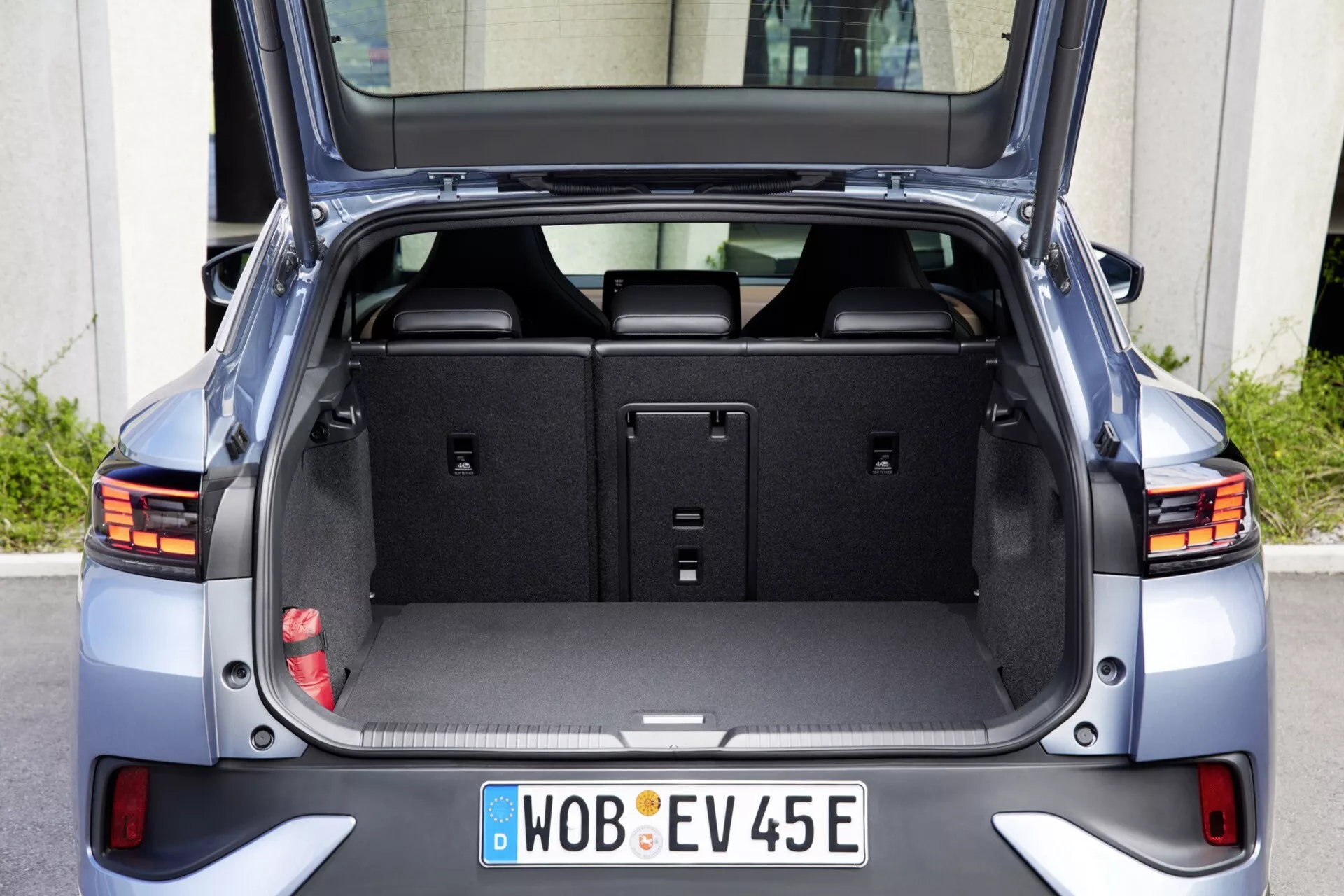 Zadní pohled na moderní hatchback VW ID.5 2022 s otevřeným kufrem, který ukazuje prostornou prázdnou úložnou oblast, čistý kobercový obklad, vztyčená zadní sedadla, integrovaná LED koncová světla, odrazky u spodního nárazníku, aerodynamický design, parkovací senzory na zadním nárazníku, evropskou poznávací značku EV a metalický povrch za denního světla.