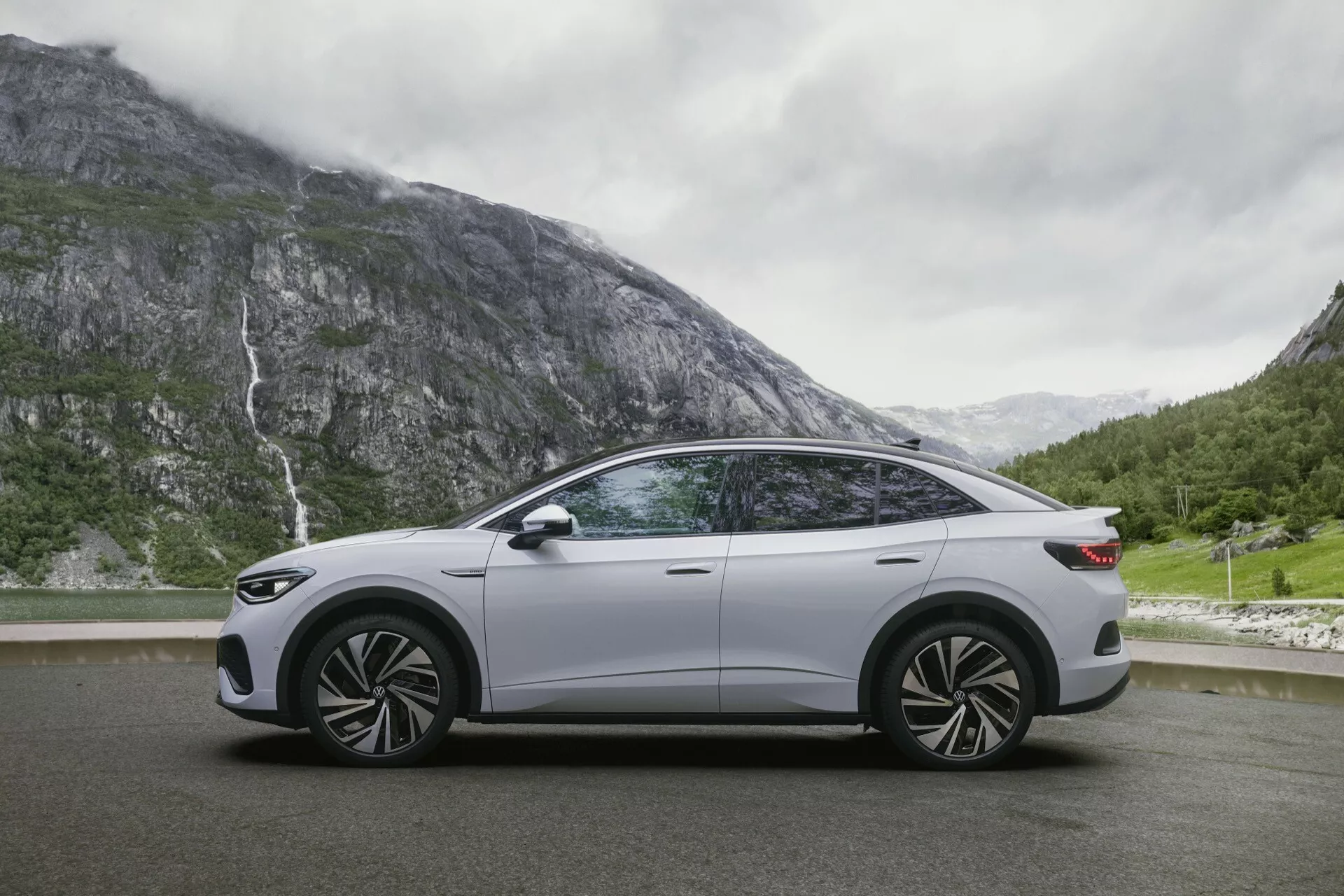 Boční profil vozu Volkswagen ID.5 2022 (1. generace), s elegantním moderním designem a detailními koly na malebné silnici s horami a vodopádem v pozadí, zdůrazňující jeho pokročilé a luxusní vlastnosti.