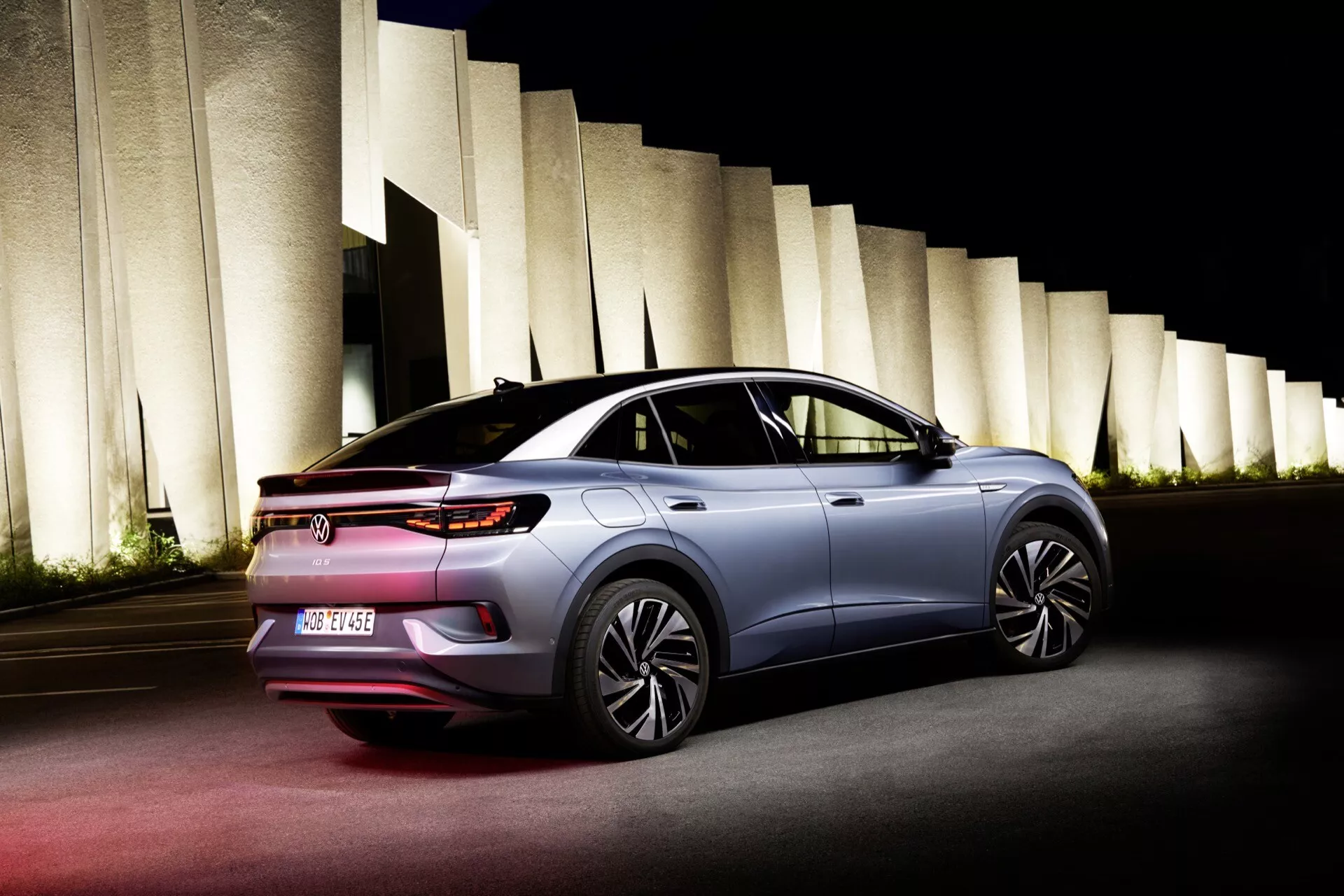 Zadní pohled z tří čtvrtí na VW ID.5 2022 (1. generace), ukazující elegantní siluetu, střechu připomínající kupé, LED zadní světla, aerodynamická boční zrcátka a moderní kola, vyfotografovaný v noci s umělým osvětlením, které zdůrazňuje vozidlo a architektonické prvky v pozadí.