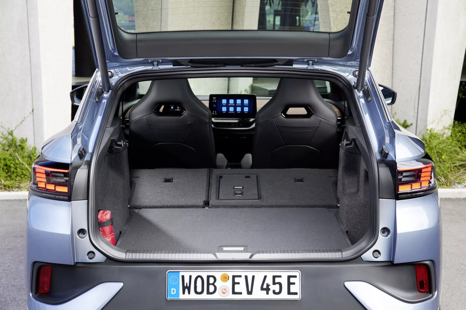 Zadní pohled na Volkswagen ID.5 2022 (první generace) s otevřeným kufrem, ukazující prostornou kapacitu nákladu s sklopenými zadními sedadly, čalouněný interiér, zasunutý zatahovací kryt nákladu, zadní okno s topnými prvky, zadní stěrač, částečně viditelné moderní LED zadní světla a registrační značku EV z Německa z Wolfsburgu, naznačující design elektrického vozidla a všestranné uspořádání nákladu.