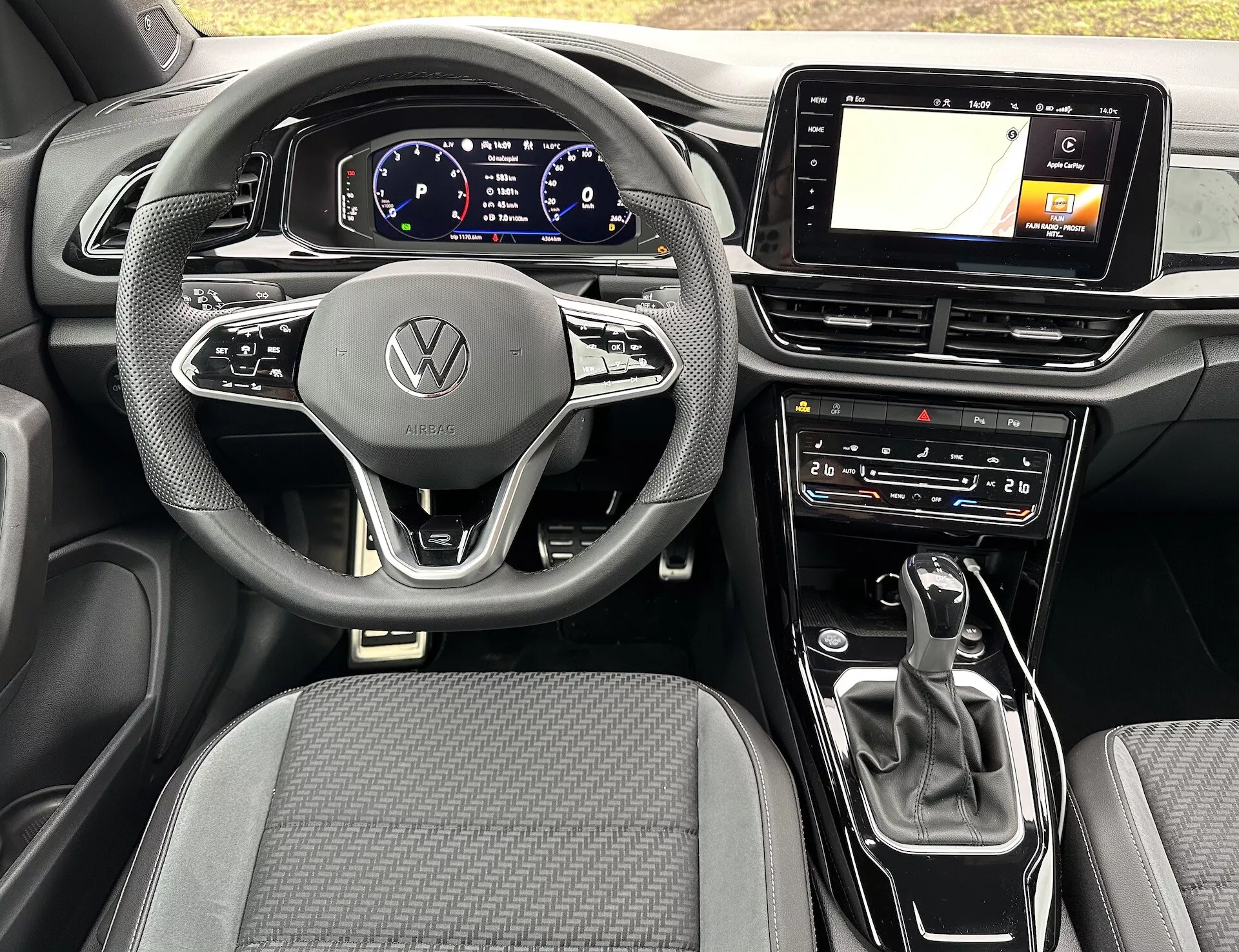 Interiér VW T-Roc Cabriolet 2022 s moderním volantem se třemi rameny s emblémem Volkswagen, digitálním přístrojovým panelem, dotykovou obrazovkou pro infotainment s GPS, voličem rychlostních stupňů automatické převodovky a ovládáním klimatizace, který zdůrazňuje pokročilou technologii a elegantní design vozu