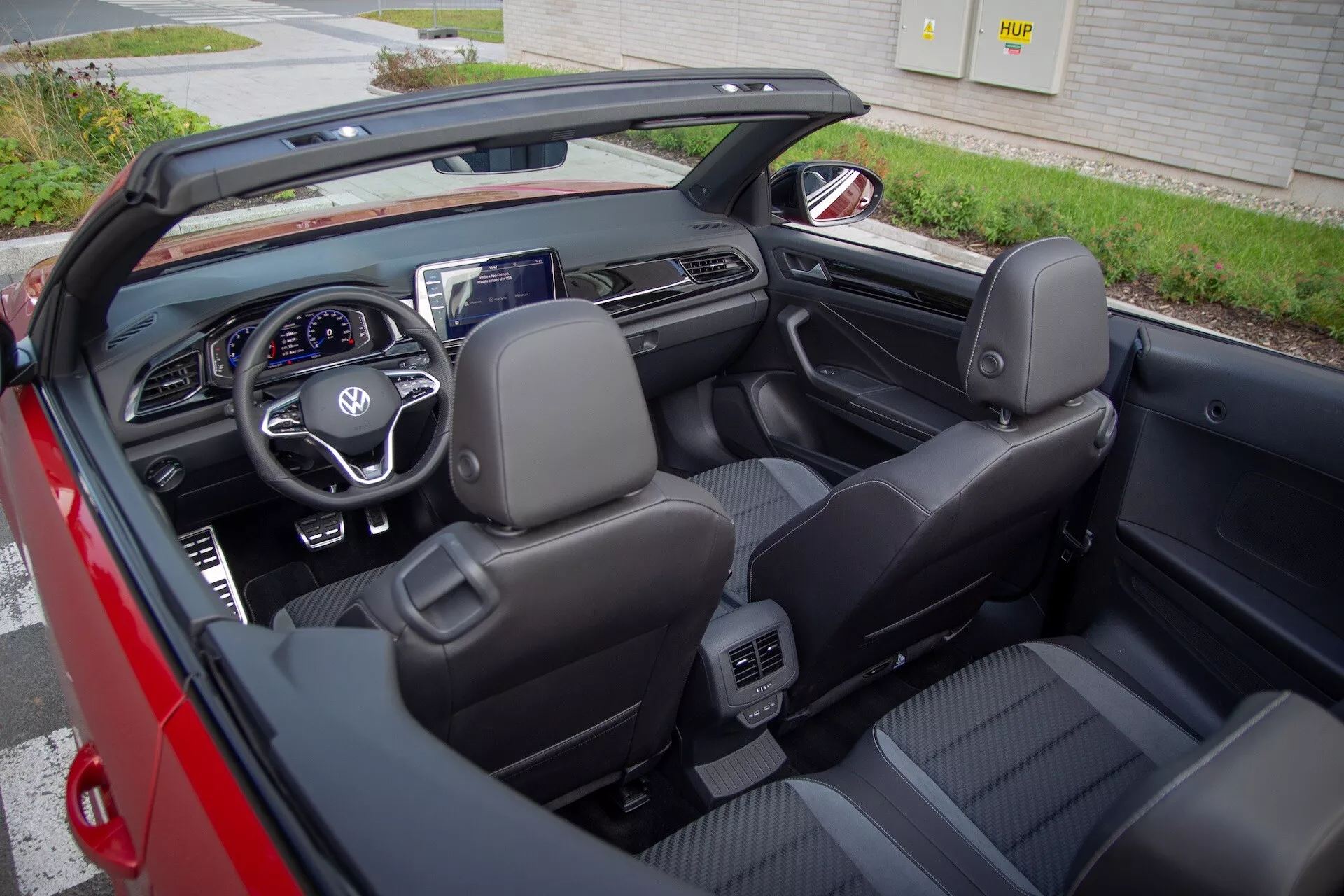 Interiérový pohled na kabriolet VW T-Roc 2022 s odnímatelnou střechou, černá kožená sedadla, multifunkční volant, digitální přístrojová deska a centrální displej infotainmentu z mírně pravého úhlu z nadhledu