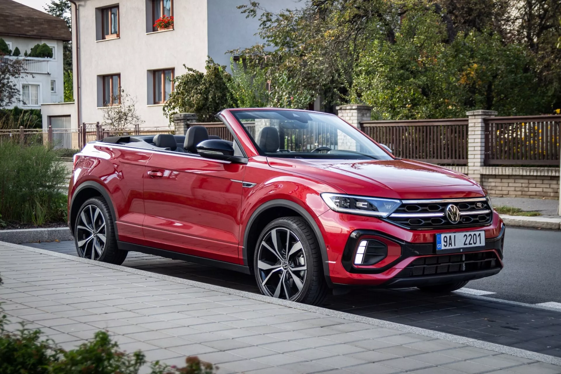 Červený kabriolet VW T-Roc 2022, ukazující jeho dynamický design s dlouhou svažující se kapotou, moderní přední mřížkou, štíhlými světlomety a aerodynamickým profilem zachyceným z částečného předního pohledu na ulici