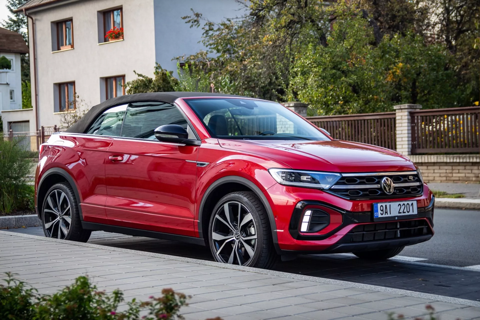VW T-Roc Cabriolet 2022 v červené barvě, ukazující jeho moderní kompaktní SUV design se zaměřením na přední blatník, sestavu LED světlometů, mřížku s chromovanou lištou, přední nárazník s možnými adaptivními funkcemi, dveře spolujezdce a slitinová kola, zaparkované na městské ulici.