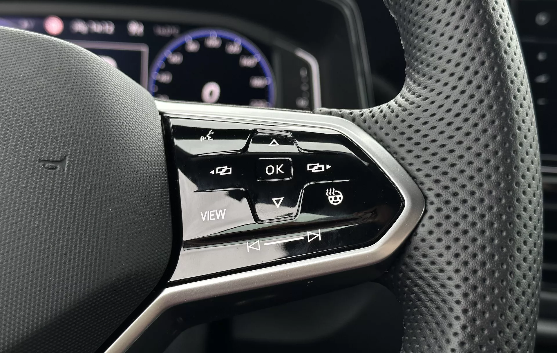 Detailní záběr na multifunkční ovládání volantu vozu VW T-Roc Cabriolet 2022, předvádějící ergonomický design a interaktivní tlačítka pro informačně-zábavní systém a nastavení vozidla
