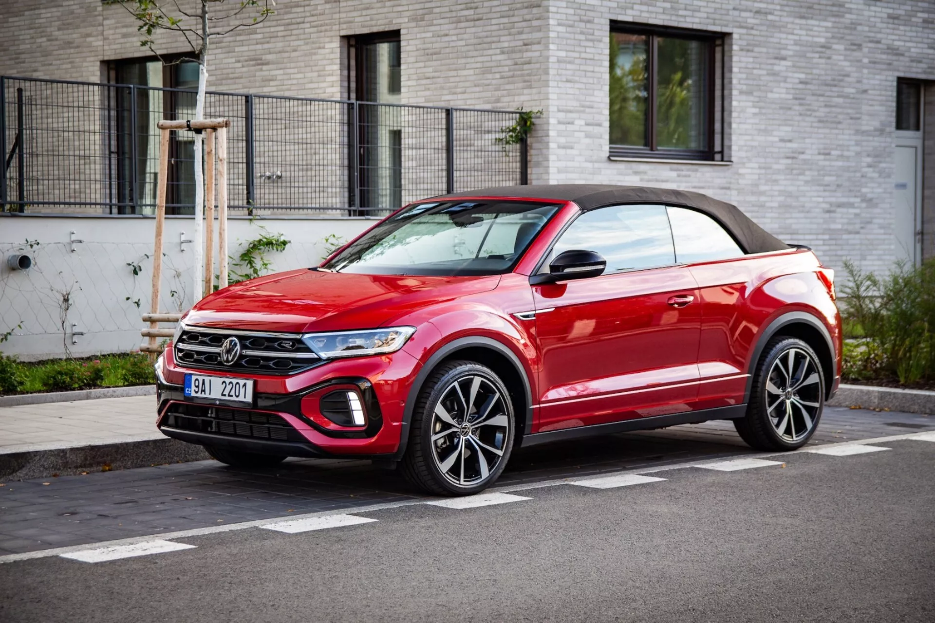 Jasně červené kabriolet crossover SUV VW T-Roc 2022 parkováno u silnice, ukazuje na přední mřížku, LED světlomety, slitinová kola a měkkou střechu, ve tříčtvrtečním pohledu zepředu za jasného počasí