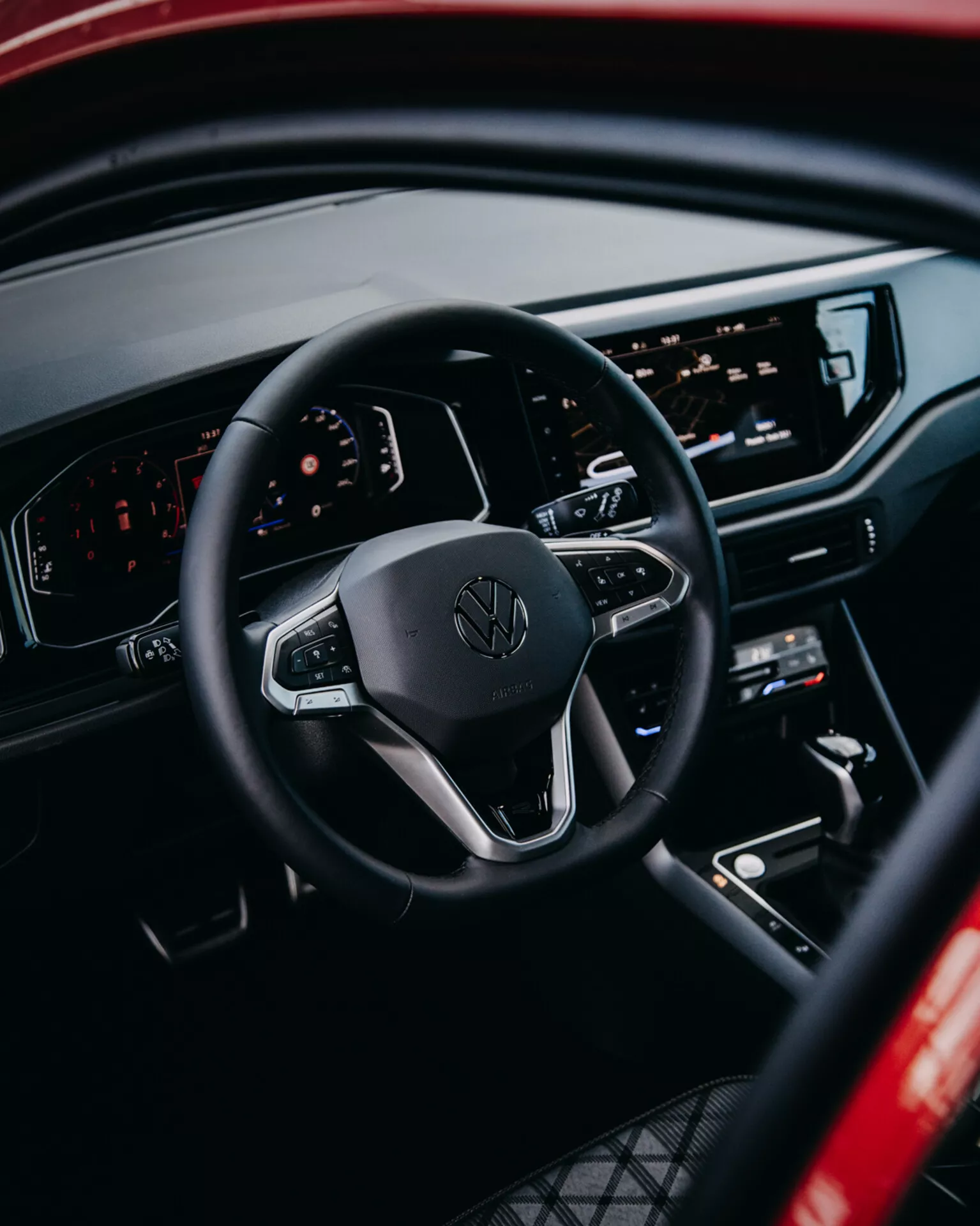 Pohled do interiéru Volkswagen Taigo 2021 s důrazem na volant s ovládacími prvky, digitální palubní desku a centrální infotainmentovou konzolu z perspektivy zadního pasažéra