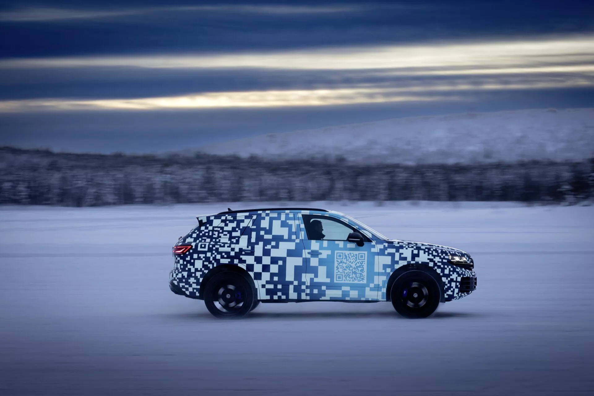 VW Touareg 2023 (III-facelift) v pohybu, zdůrazňující jeho aerodynamický design a LED zadní světla, s maskovacím polepem, v zimním testovacím prostředí