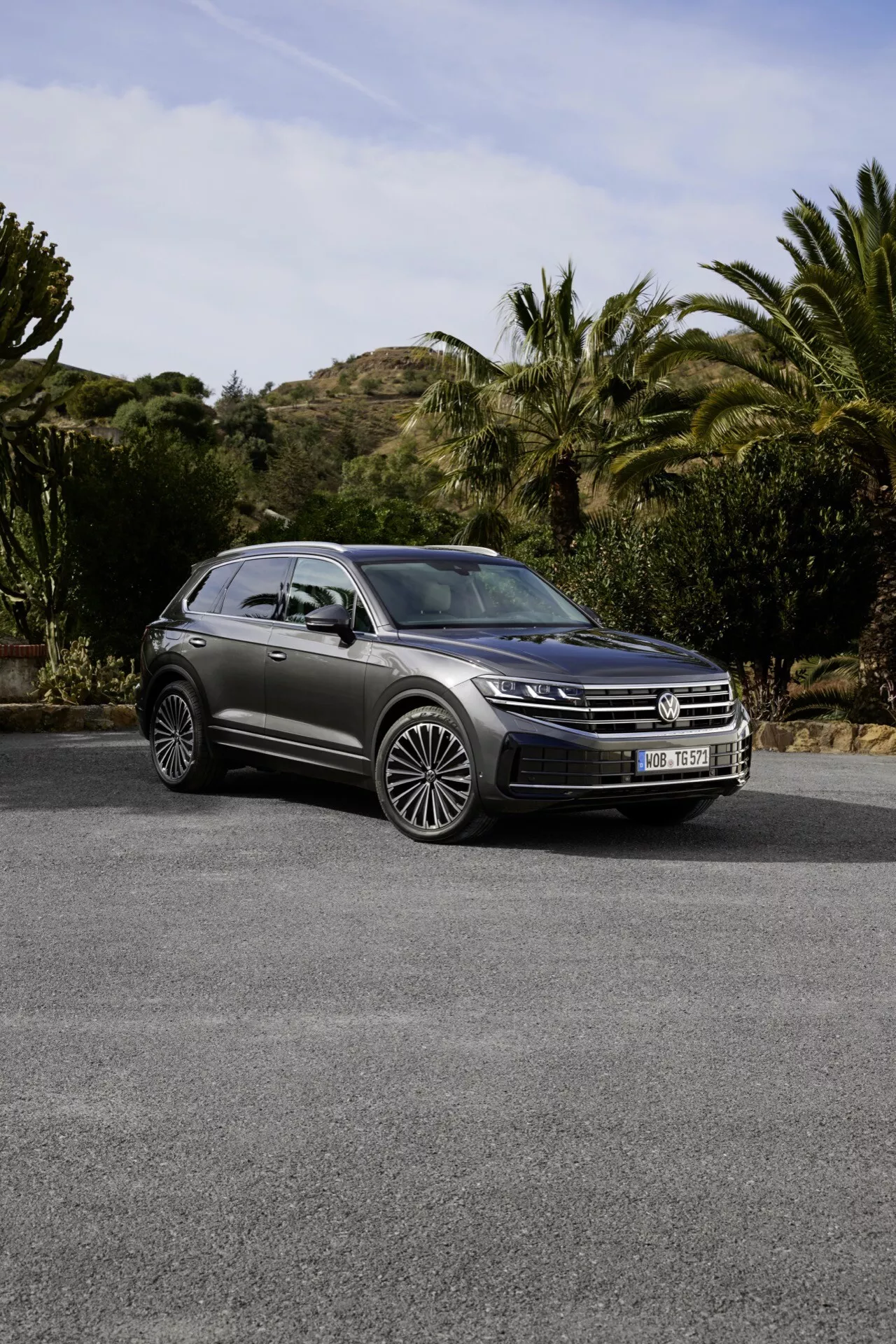Model VW Touareg III facelift 2023 zaparkovaný venku s přední mřížkou, LED světlomety, panoramatickou střechou a vícepaprskovými slitinovými koly na pozadí malebných kopců, keřů a stromů, což zdůrazňuje jeho luxusní SUV design a pokročilé funkce.