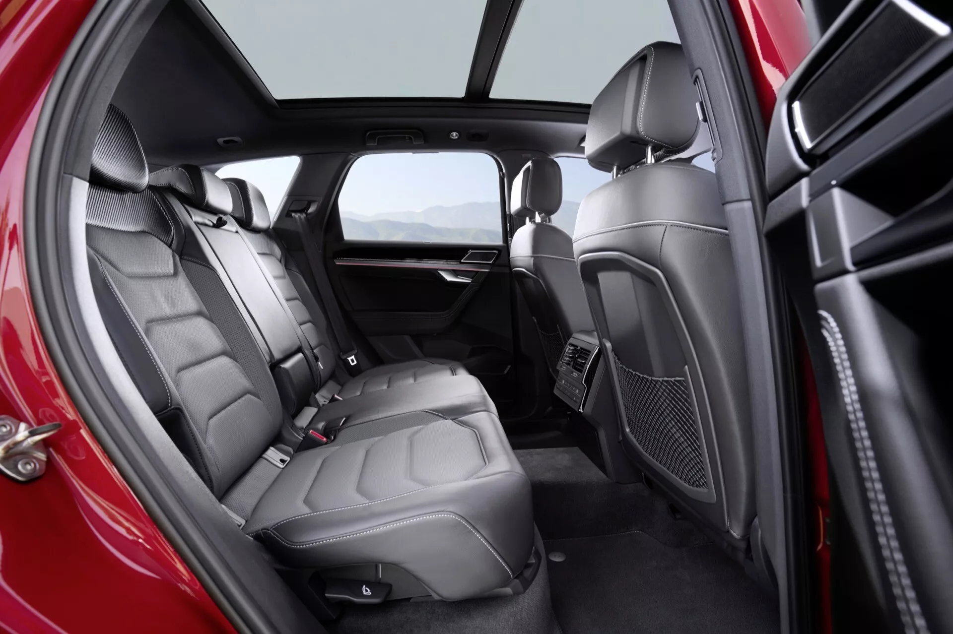 Snímek interiéru Volkswagen Touareg (III Facelift) 2023 zobrazující luxusní zadní oddíl pro cestující s prémiovými koženými sedadly, integrovaným zábavním systémem, panoramatickým střešním oknem a sofistikovanými designovými prvky z perspektivy diváka z pravé strany
