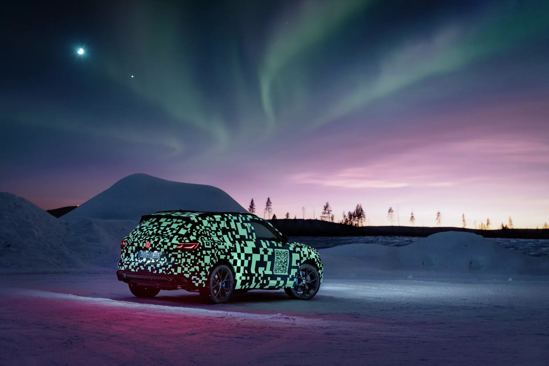 Prototyp VW Touareg (III-Facelift) 2023 v maskovacím obalu zachycený z bočního profilu na sněhovém podkladu s ambientním osvětlením zdůrazňujícím vozidlo proti pozadí polární záře a soumrakových odstínů, naznačující elegantní, možná elektrický, hatchback nebo crossover design