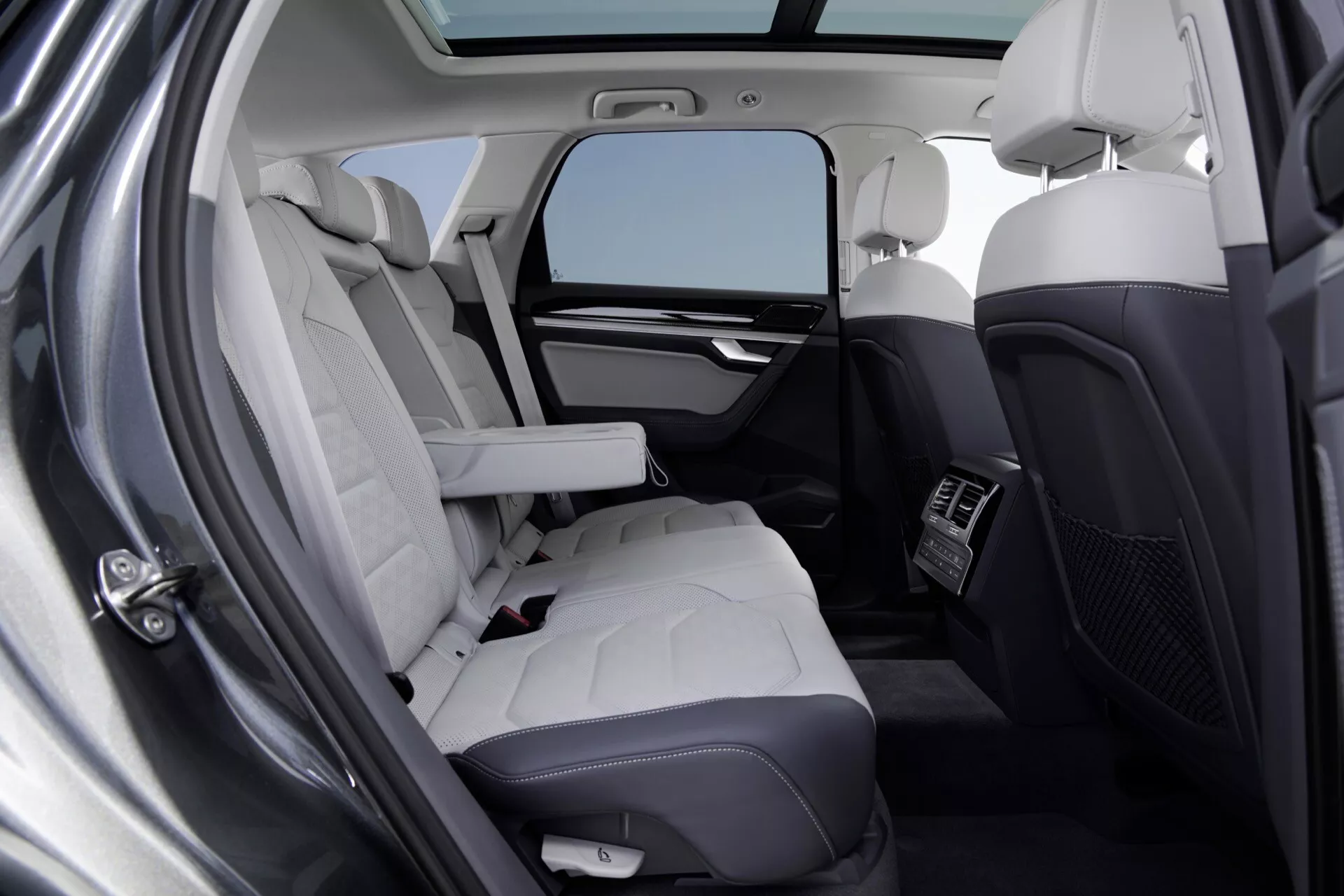 Interiér VW Touareg 2023 (III Facelift) ukazující luxusní zadní sedadla s prošívanými sedáky v světlé kůži, integrované technologické funkce a osvětlení panoramatickou střechou