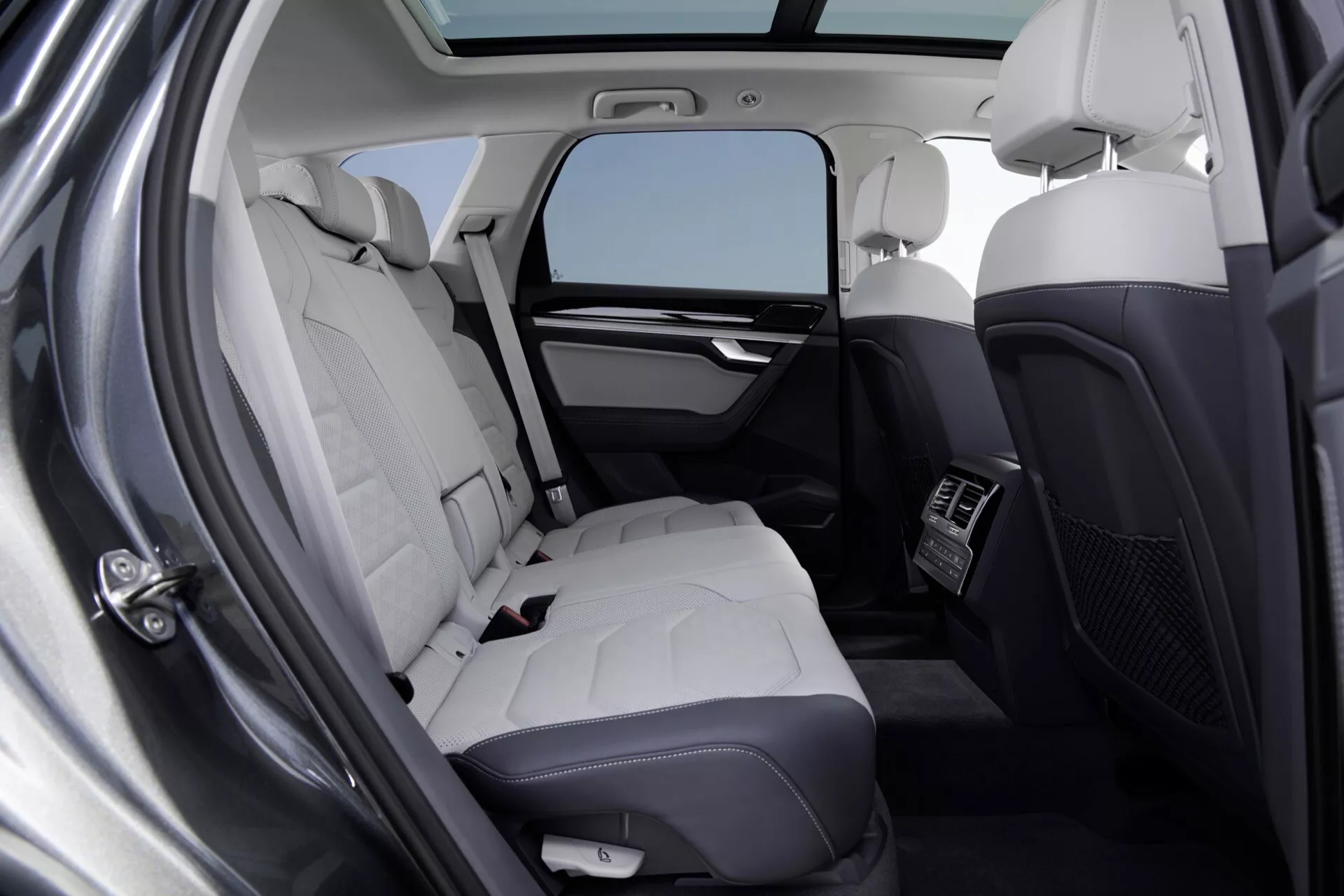 Pohled do interiéru VW Touareg 2023 (III-Facelift) se zaměřením na luxusní zadní sedadla s čalouněním z jasně barevné kůže, klimatizací a prémiovými detaily kabiny z perspektivy otevřených zadních levých dveří.