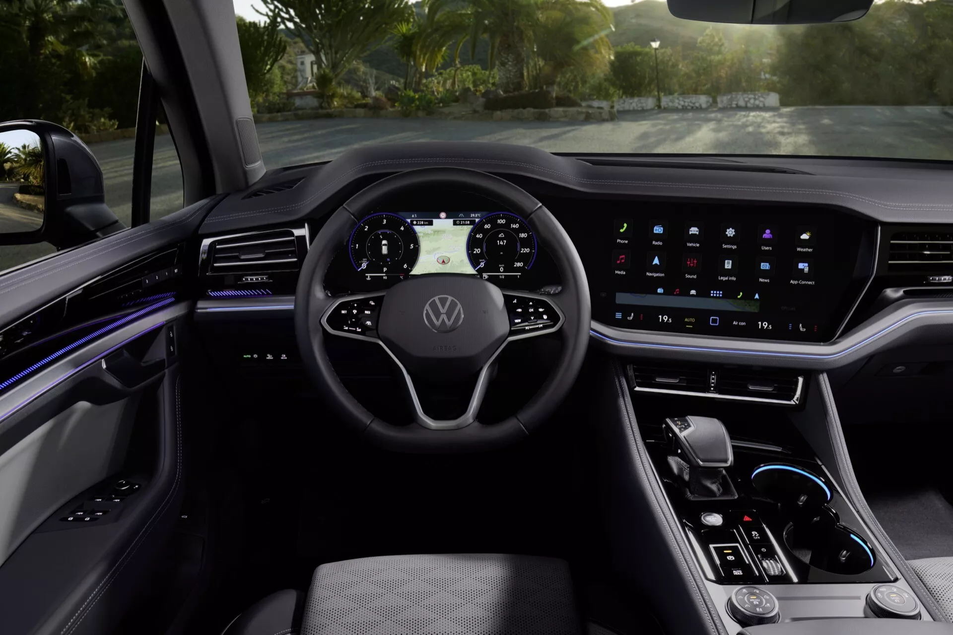 Interiér VW Touareg 2023 z pohledu řidiče s moderním volantem se třemi paprsky s logem Volkswagen, digitálním přístrojovým panelem, širokou dotykovou obrazovkou informačního systému, ambientním osvětlením, elegantní středovou konzolou s volbou převodovky a prvotřídními materiály
