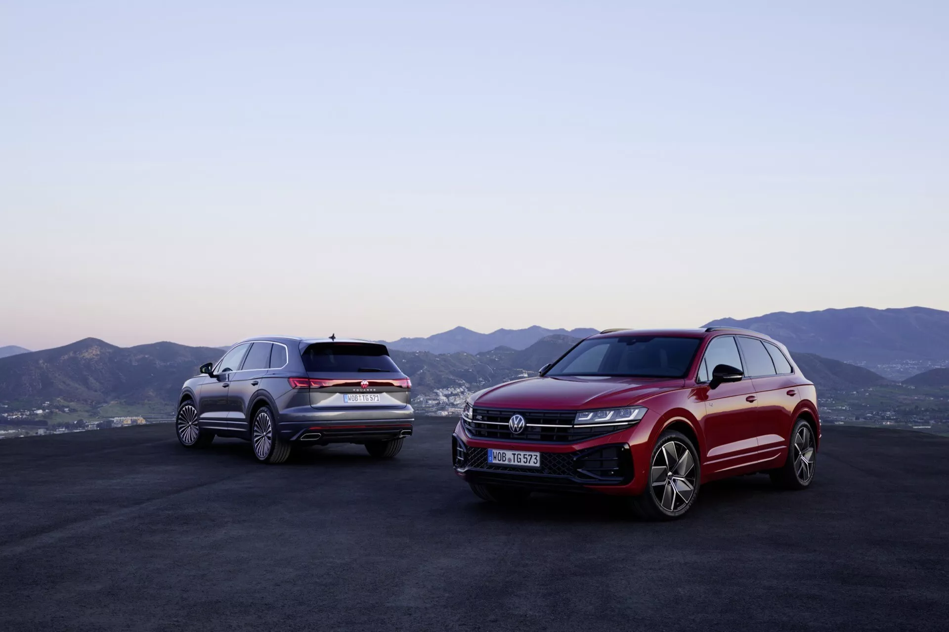 Modely Volkswagen Touareg (III-facelift) 2023 v červené a stříbrné barvě v exteriéru s horským panoramatem a soumrakovým nebem, předvádějící přední a boční profily s pokročilou technologií LED osvětlení