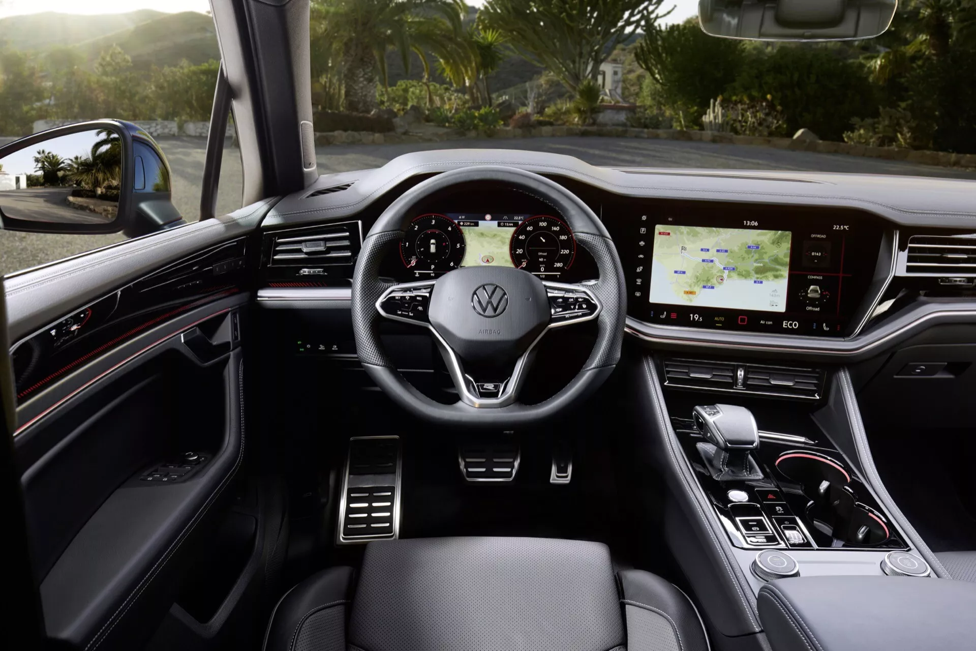 Vnitřek VW Touareg 2023 s pohledem na multifunkční volant obalený kůží s logem Volkswagen, digitálním palubním počítačem, dotykovým infotainment systémem a elegantní voličem převodů v luxusním provedení s tmavými tóny a kovovými akcenty