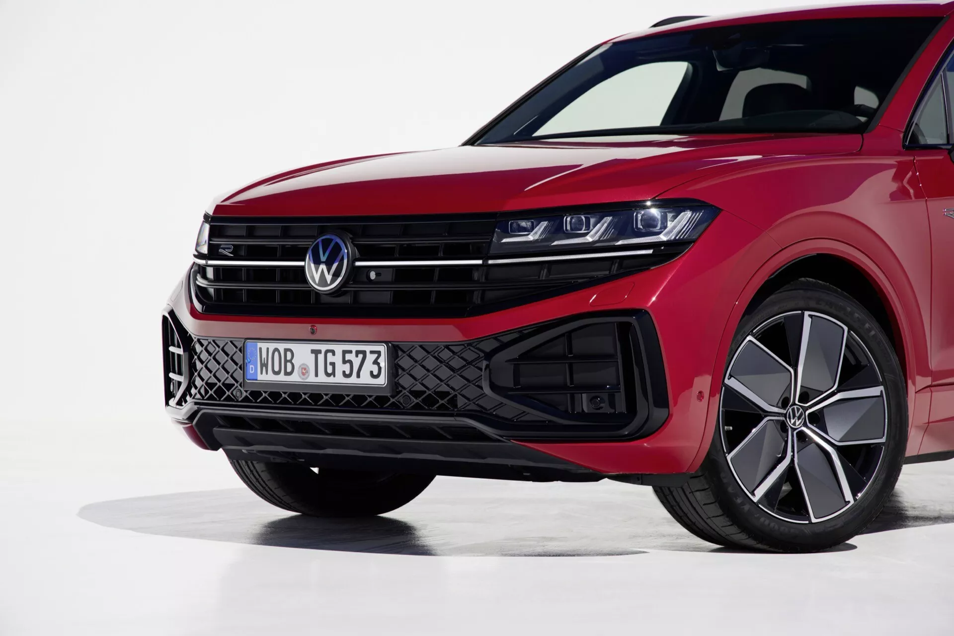 Pohled zepředu vlevo na Volkswagen Touareg 2023 zdůrazňující jeho LED světlomety, sportovní mřížku a výkonný červený lak