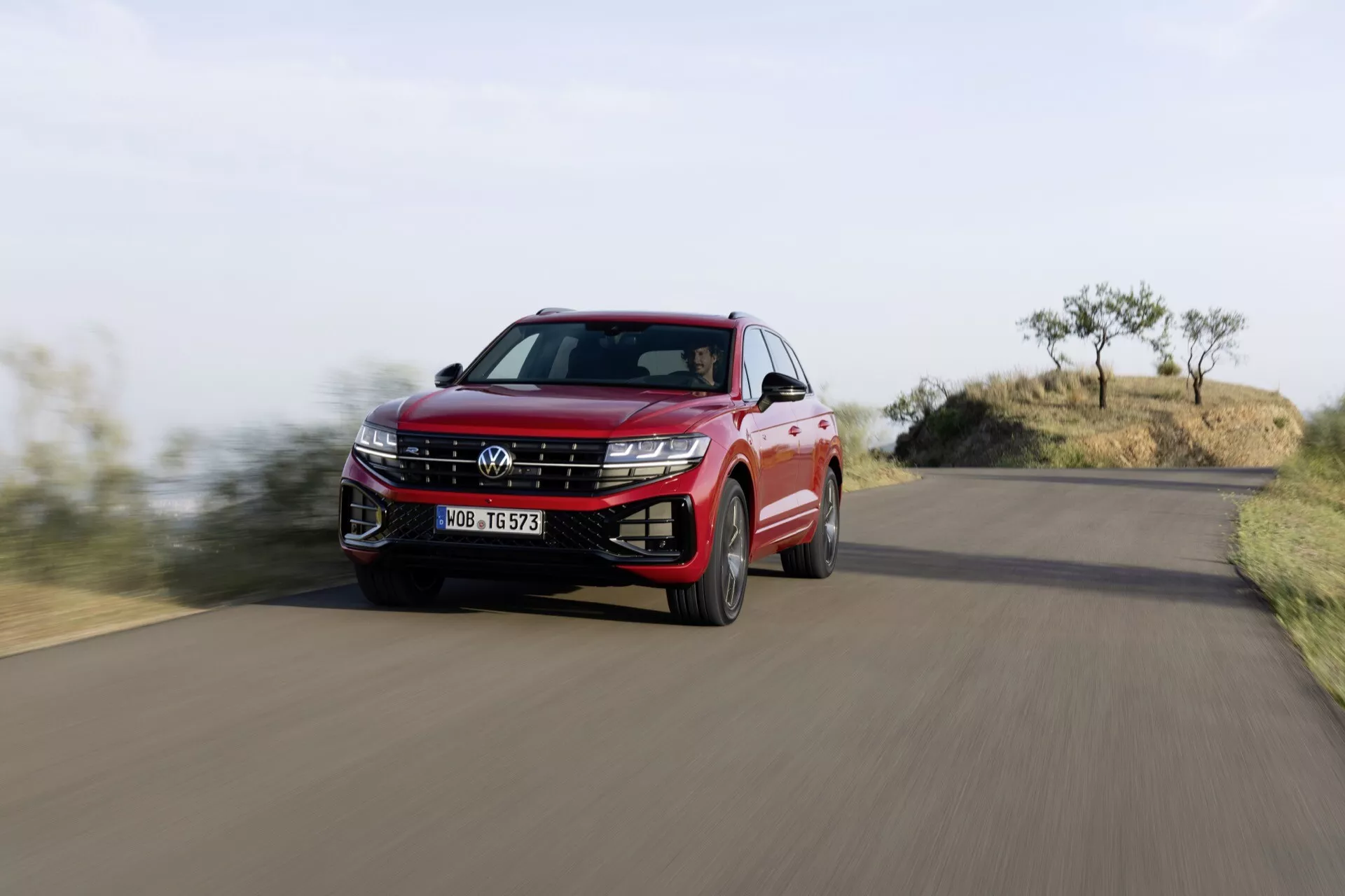 Volkswagen Touareg 2023 v červené barvě zachycený v pohybu z nízkého úhlu, zdůrazňující masku chladiče, LED světlomety a dynamický boční profil uprostřed přírodní krajiny.