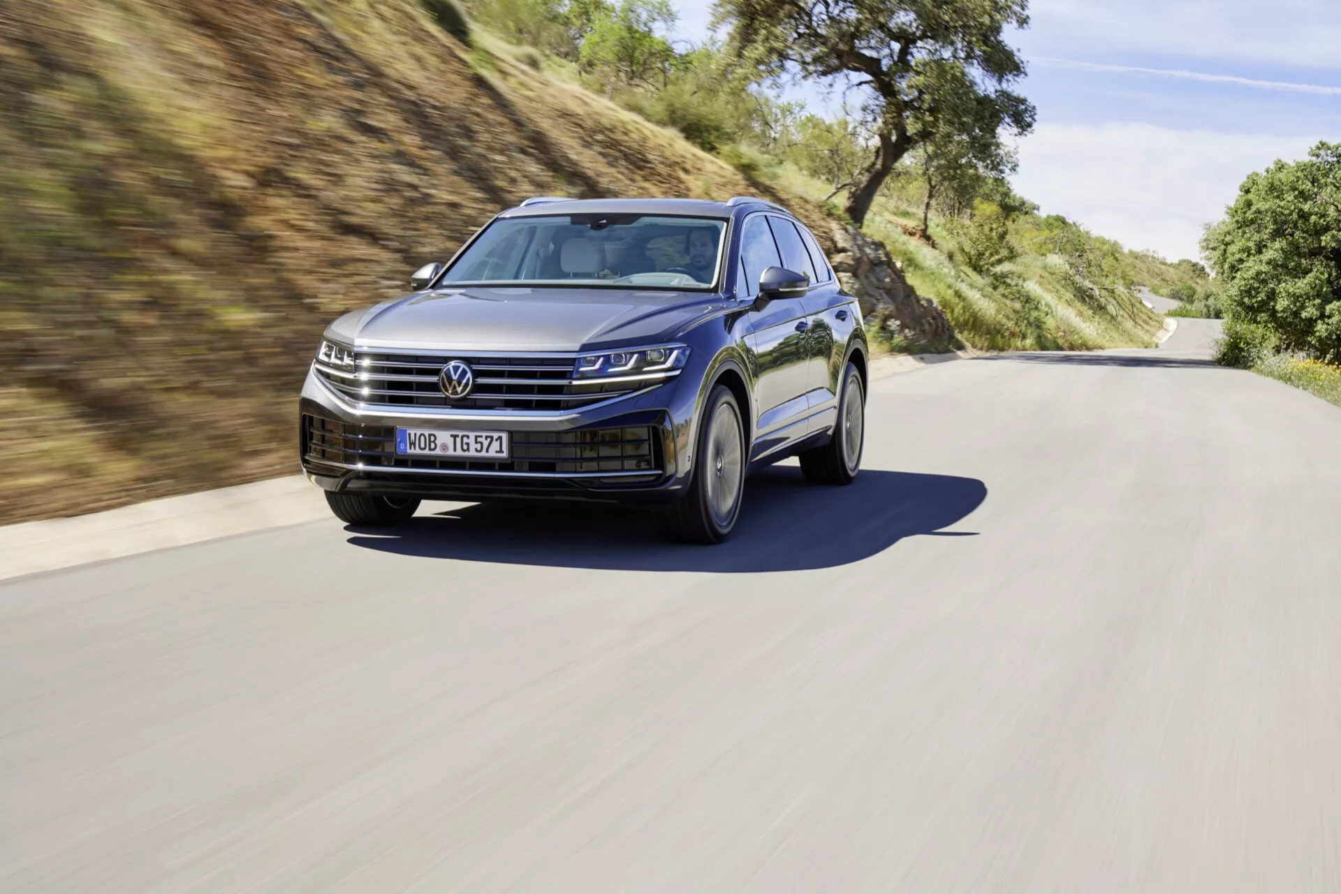 VW Touareg III facelift 2023 zobrazený v dynamickém silničním prostředí, zdůrazňující LED světlomety, moderní mřížku chladiče, sportovní slitinová kola a funkce ADAS.