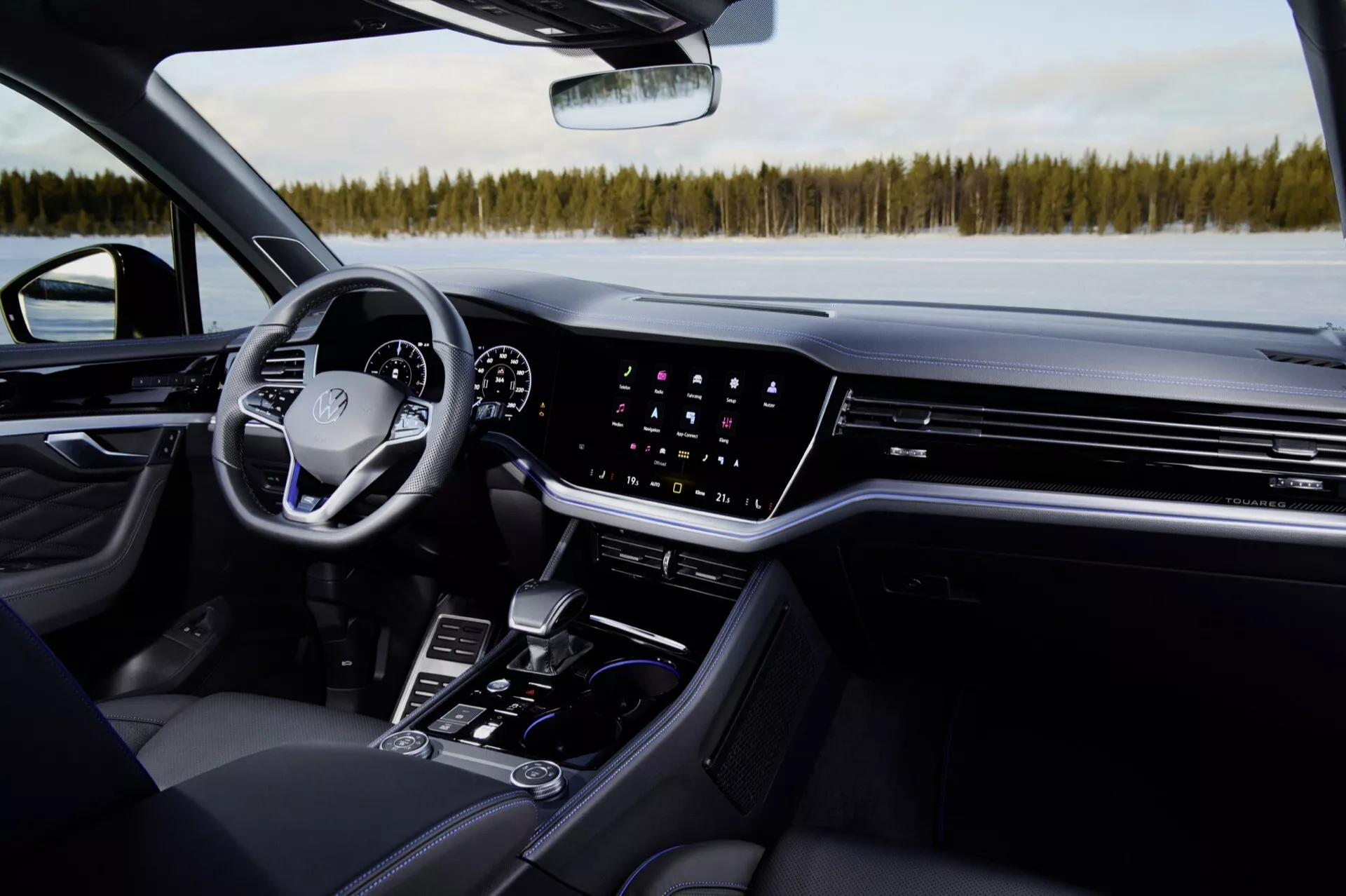 Interiér Volkswagen Touareg 2023: Pohled z perspektivy spolujezdce zdůrazňující palubní desku, dotykovou obrazovku infotainmentu, klimatizaci, digitální přístrojový panel, multifunkční volant a prvky středové konzoly v moderním luxusním automobilu