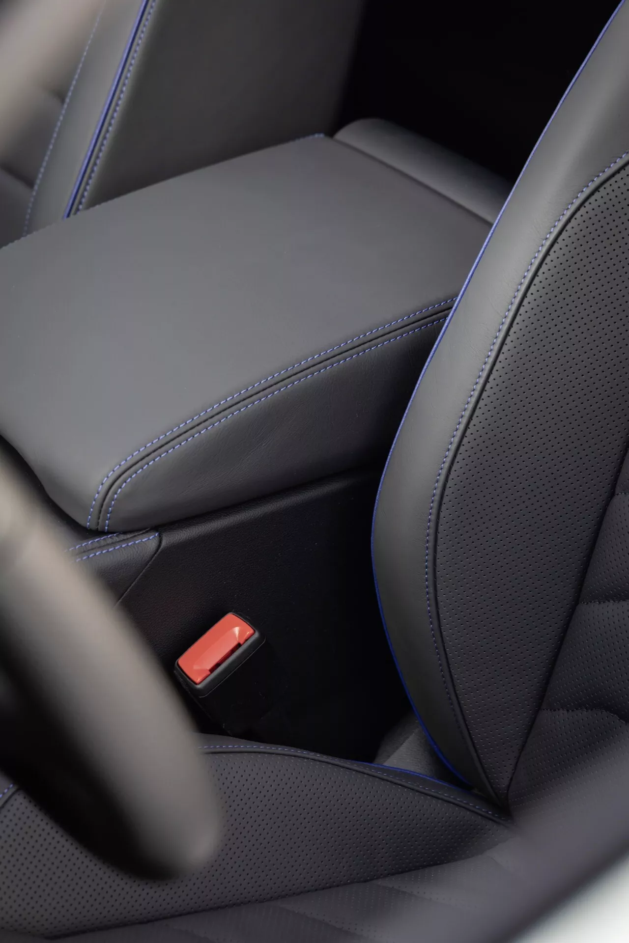 Detailní interiérový pohled na VW Touareg (III facelift) 2023 ukazující ergonomický design černého koženého sedadla se zdůrazněným prošitím, perforovaným středem pro možné vytápění/chlazení a červenou sponu bezpečnostního pásu, která zdůrazňuje luxus a bezpečnostní prvky
