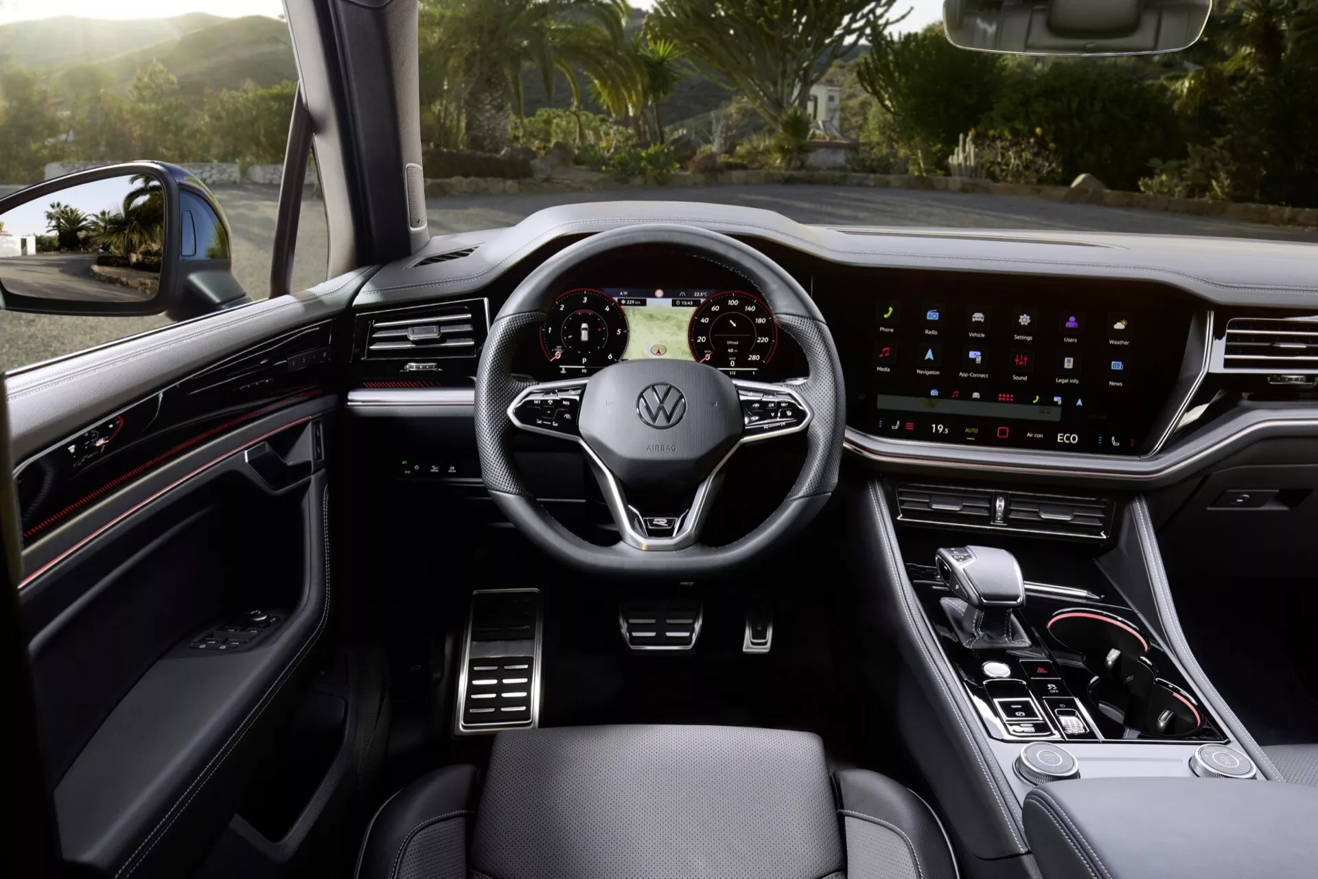 Vnitřek Volkswagen Touareg 2023 z pohledu řidiče ukazující moderní trojramenný volant s logem Volkswagen, digitální přístrojový panel, široký dotykový informačně-zábavní systém na palubní desce, minimální fyzické ovladače, páku automatické převodovky a prémiová kožená sedadla s viditelnými ovládáními